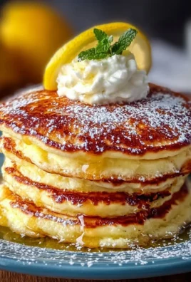 Fluffy lemon ricotta pancakes stacked on a plate with syrup and lemon slices