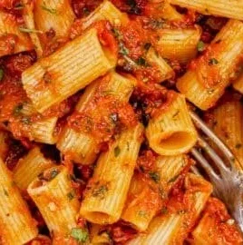 A bowl of Arrabbiata Rigatoni topped with fresh herbs and cheese