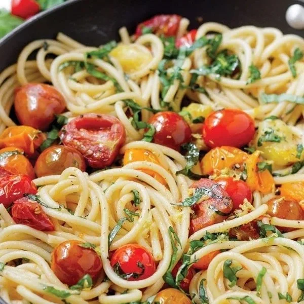 Delicious plate of tomato basil pasta topped with fresh basil and parmesan cheese.
