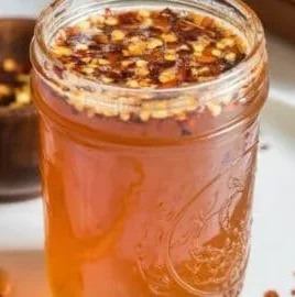 Jar of homemade hot honey with chili peppers and honey drizzling from a spoon.