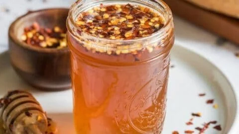 Jar of homemade hot honey with chili peppers and honey drizzling from a spoon.