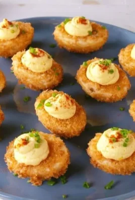 Fried deviled eggs topped with paprika and herbs on a serving platter.