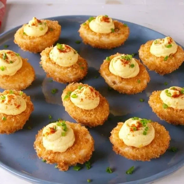 Fried deviled eggs topped with paprika and herbs on a serving platter.