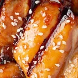 Grilled soy garlic chicken thighs on a serving plate garnished with green herbs.