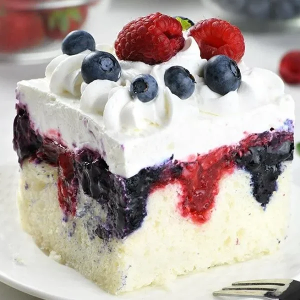 Delicious Summer Berry Poke Cake topped with fresh berries and whipped cream.